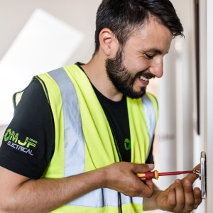 MJF Electrician wiring a light switch, smiling
