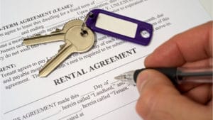 Paperwork of a Rental Agreement with Keys and A hand holding a pen signing the document